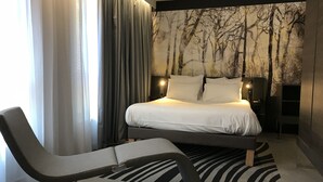 A modern bedroom with a bed, a chair, a nightstand, and a wall with a tree mural.