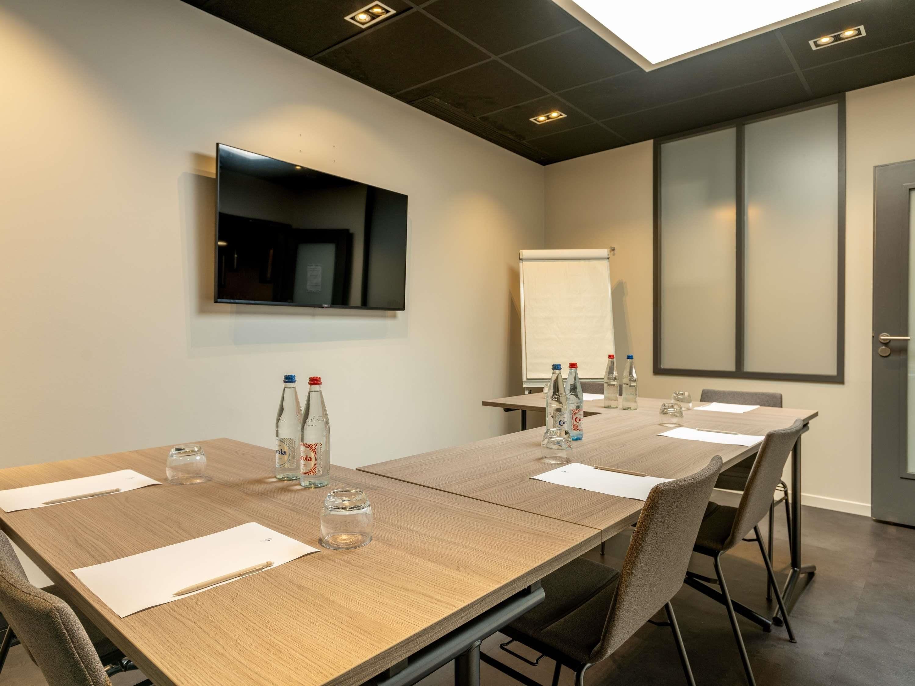 Ein Konferenzraum mit einem langen Tisch, Stühlen, einer Whiteboard und Wasserflaschen.