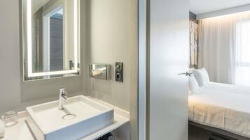 A modern bathroom with a large mirror, a white sink, and a towel dispenser.