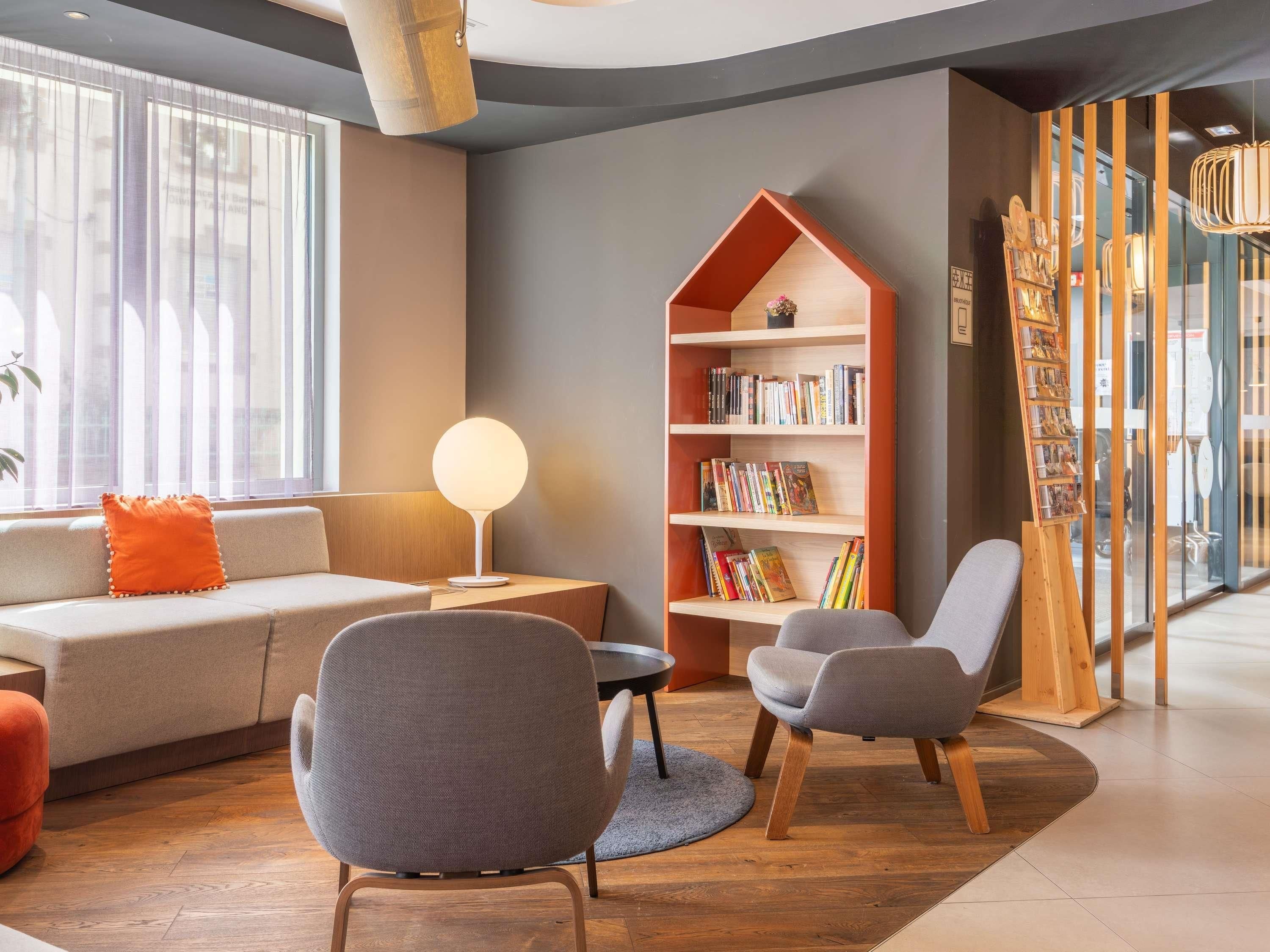 A modern living room with a sofa, two chairs, a bookshelf, and a lamp.