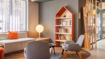 A modern living room with a sofa, two chairs, a bookshelf, and a lamp.