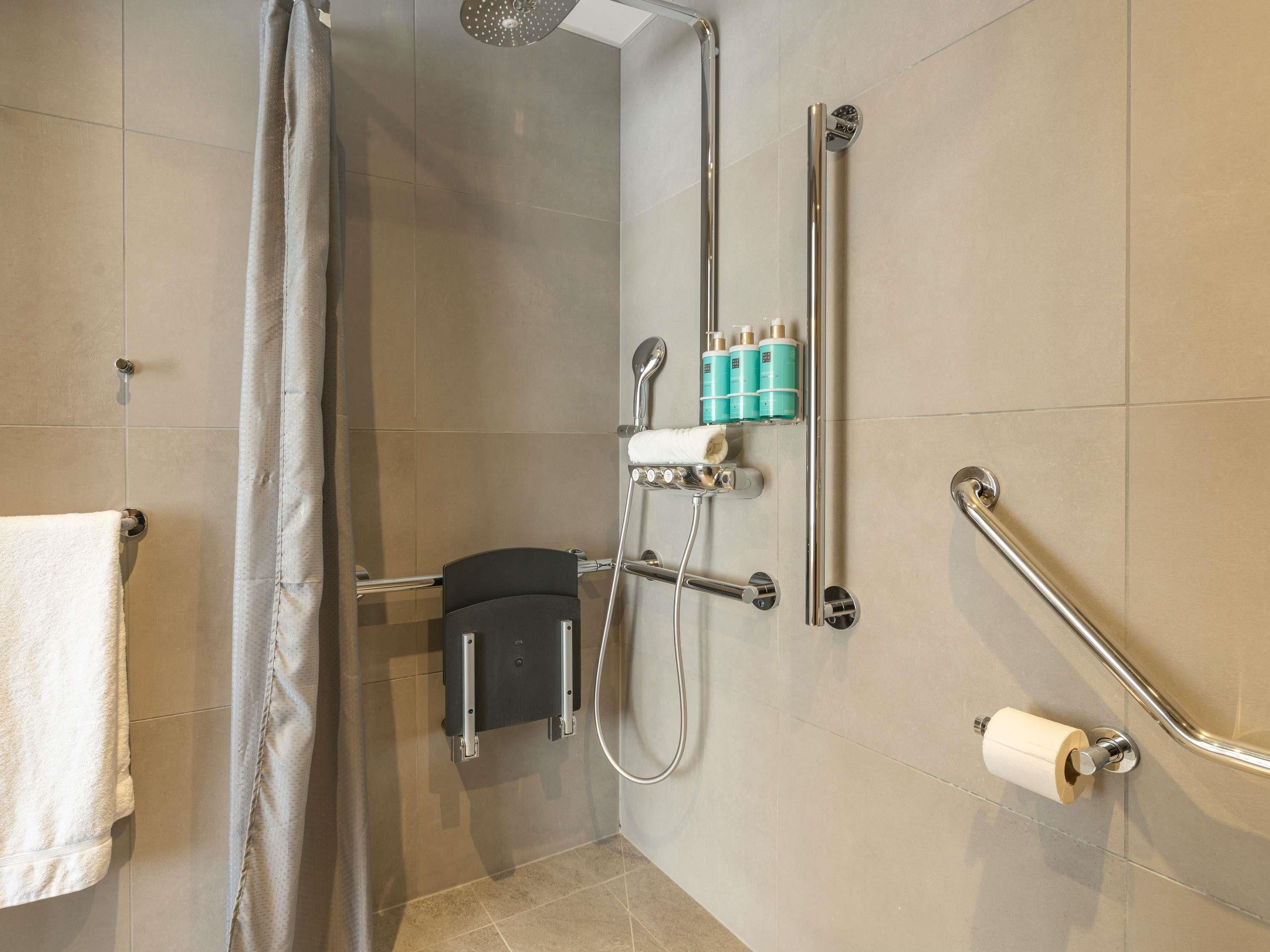 A shower area with a glass door, a towel rack, a handrail, and a toilet paper holder.