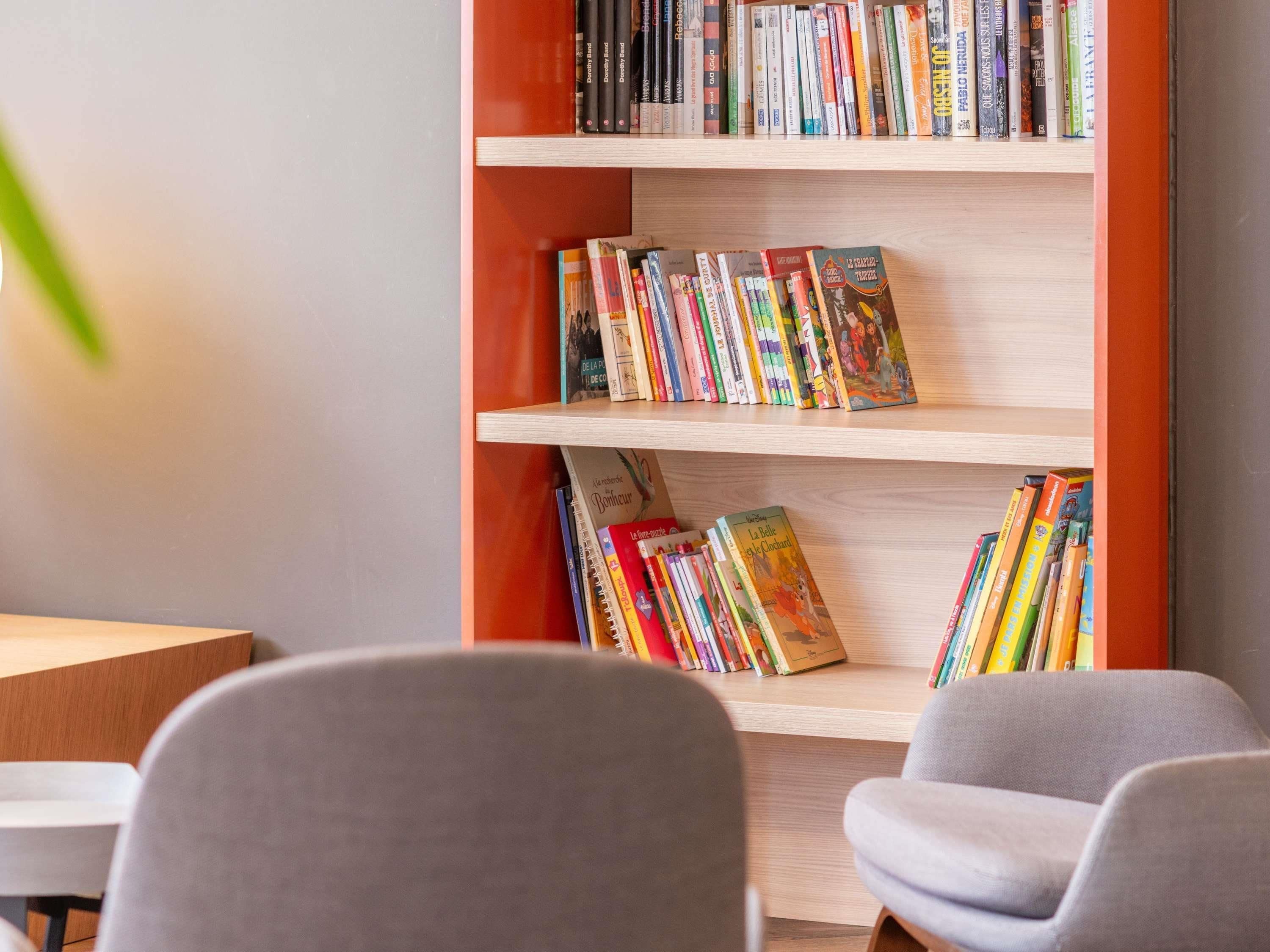 Una estantería con varios libros, un sillón gris y una mesa de madera.