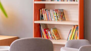 Una estantería con varios libros, un sillón gris y una mesa de madera.
