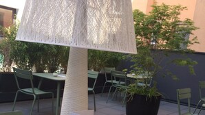 Un área de estar al aire libre con mesas y sillas verdes, una lámpara decorativa y plantas en macetas.