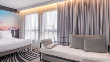 Une chambre d’hôtel moderne équipée d’un lit, d’un canapé et de grandes fenêtres avec des rideaux.