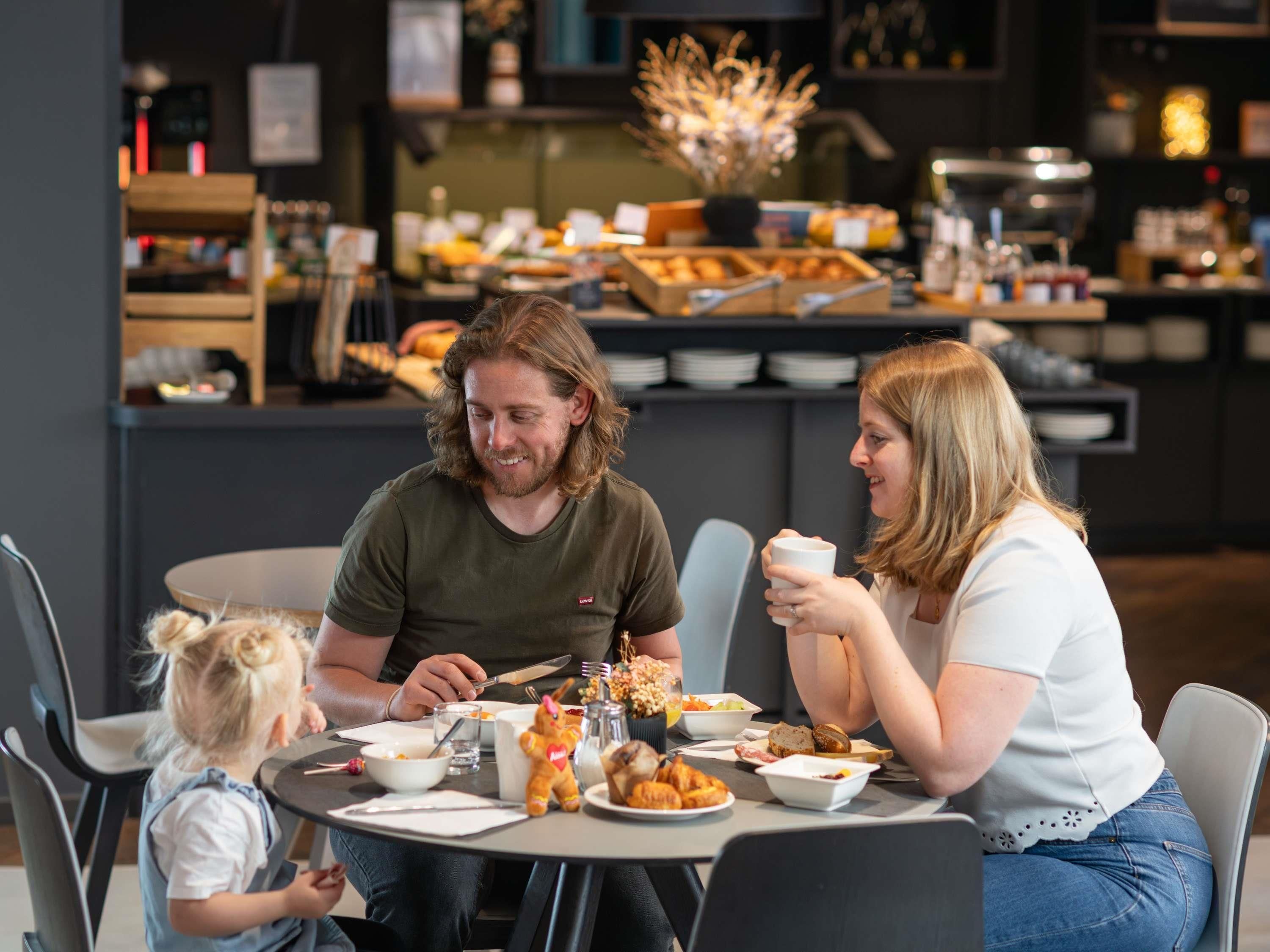 Una familia cenando en una mesa con diversos platos, un niño y una zona de cocina al fondo.