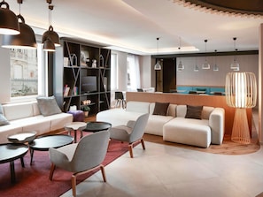 Um lobby de hotel moderno com um sofá, cadeiras, uma televisão e uma área de refeições.