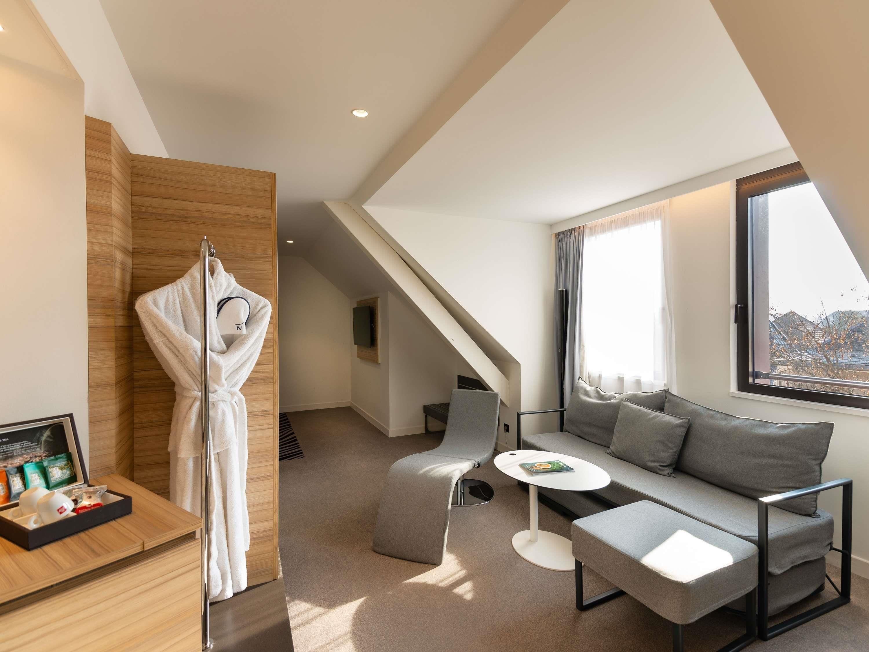 A modern hotel room with a sofa, a small table, a robe, and a framed picture on a wooden sideboard.