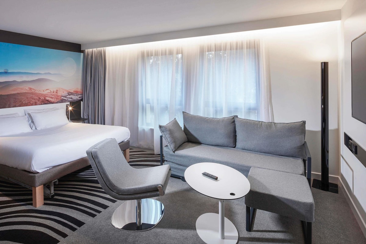 Una habitación de hotel con cama, sofá, una mesita redonda y televisor.