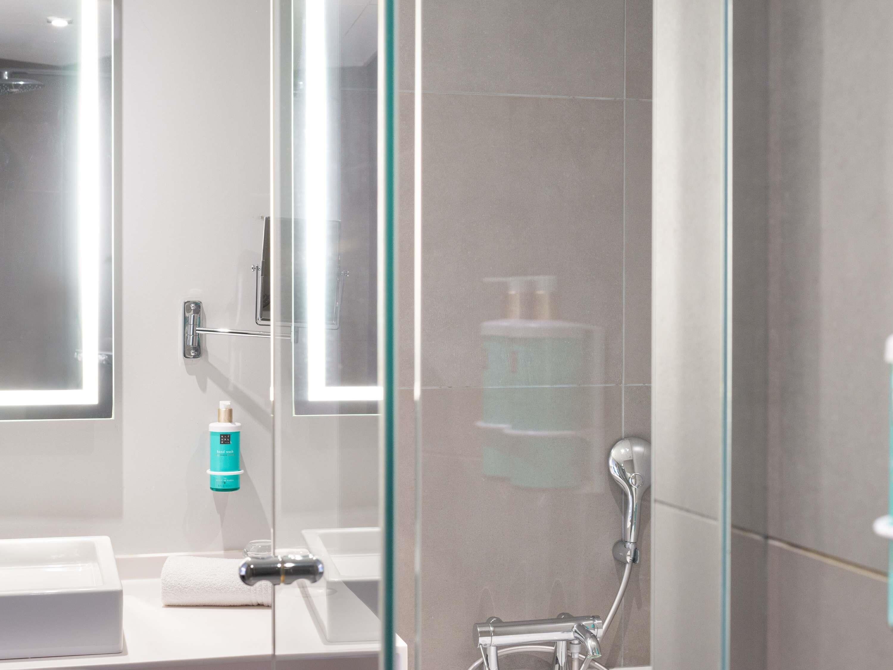 Un bagno moderno con cabina doccia in vetro, lavandino bianco e porta asciugamani.