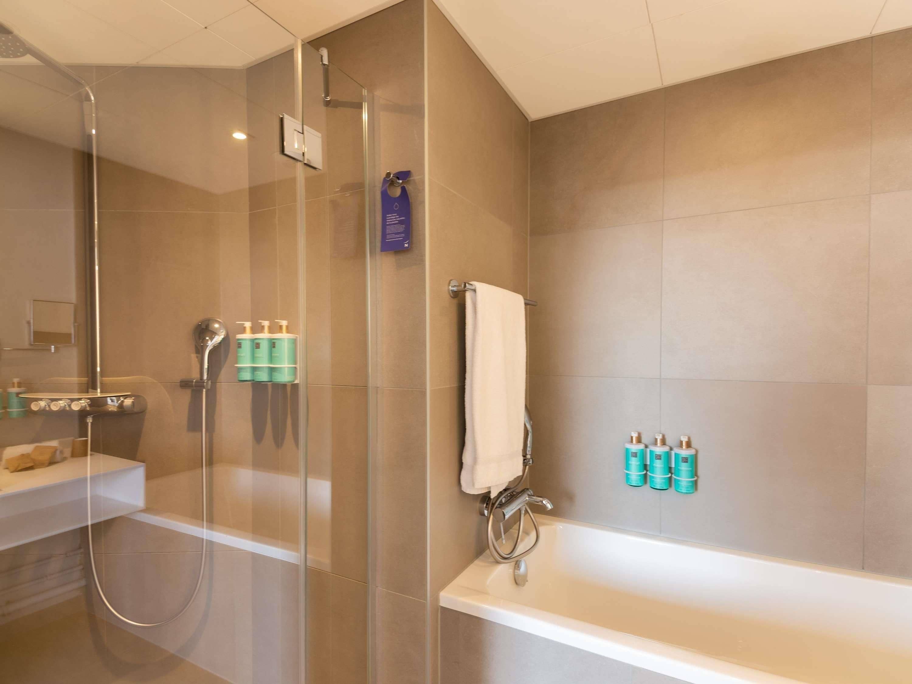 Ein modernes Badezimmer mit einer Glasdusche, einer Badewanne und Pflegeprodukten an der Wand.