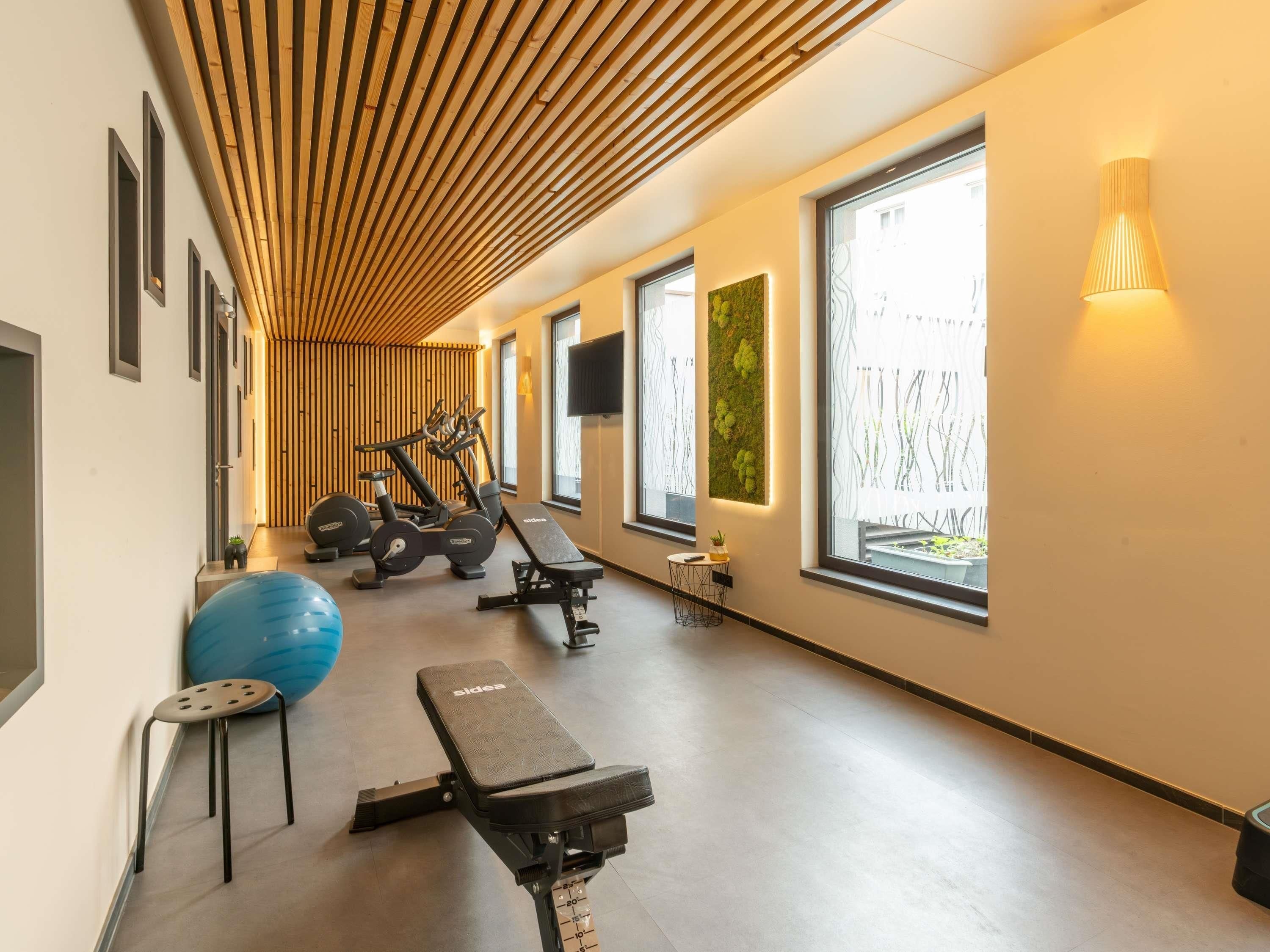Un gimnasio con equipo de ejercicio, una banca y ventanas amplias.