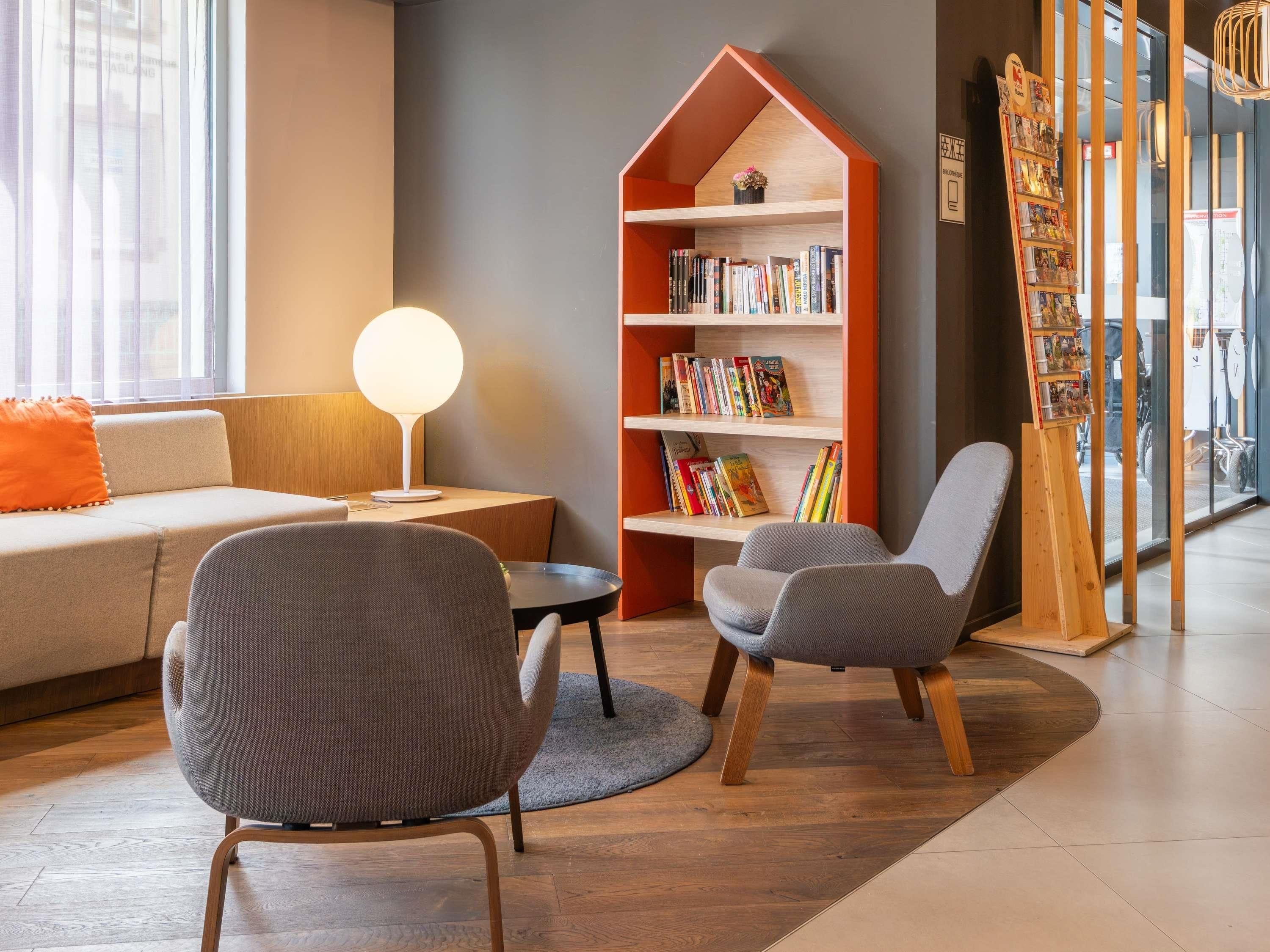 Un espace de lecture moderne comprenant un canapé, des fauteuils, une bibliothèque et une lampe.