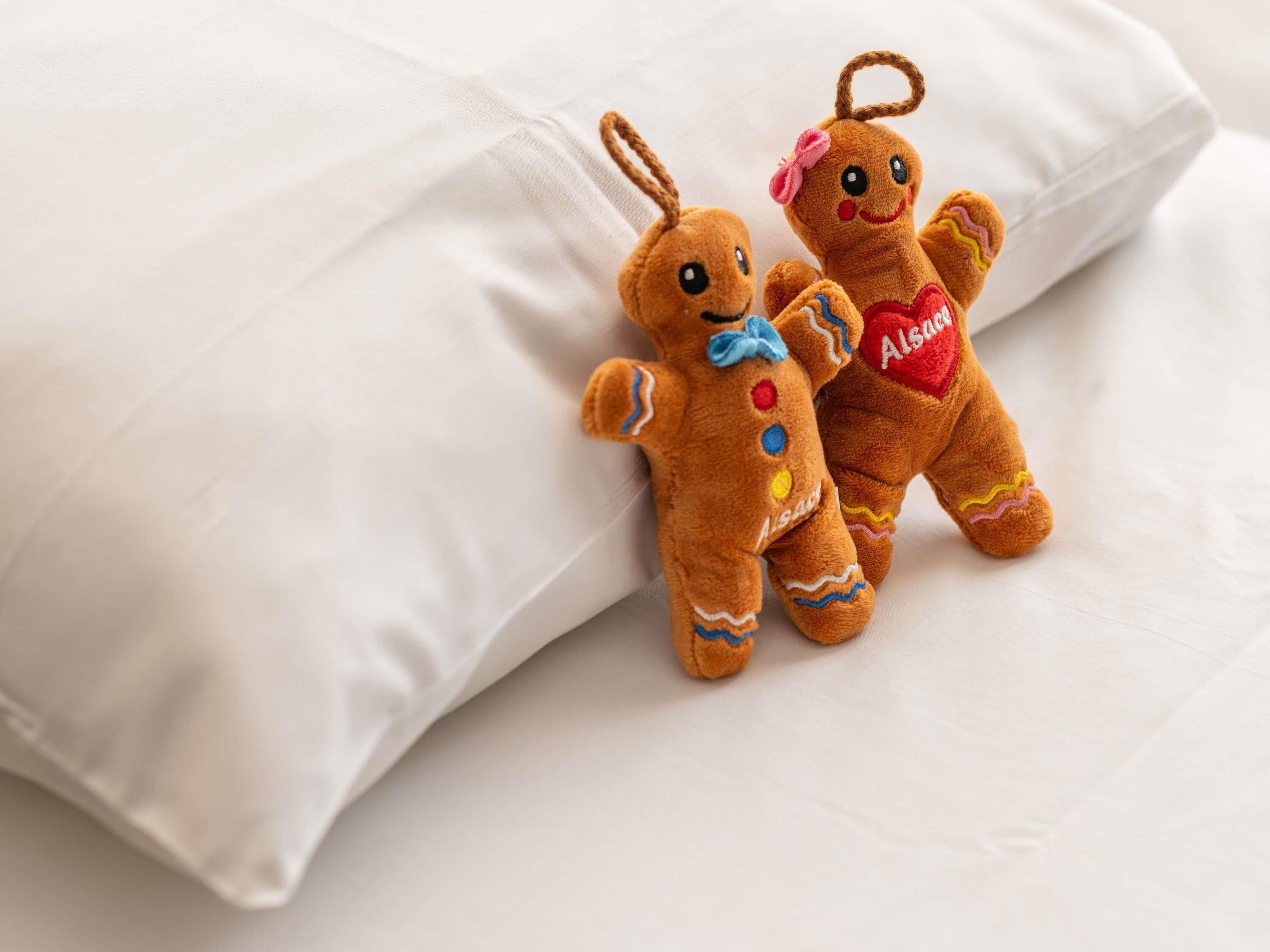 Two gingerbread man plush toys on a white pillow.