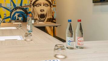Habitación de hotel con una mesa de madera, dos botellas de agua, un vaso y una placa con el nombre 'NOVOTEL'.