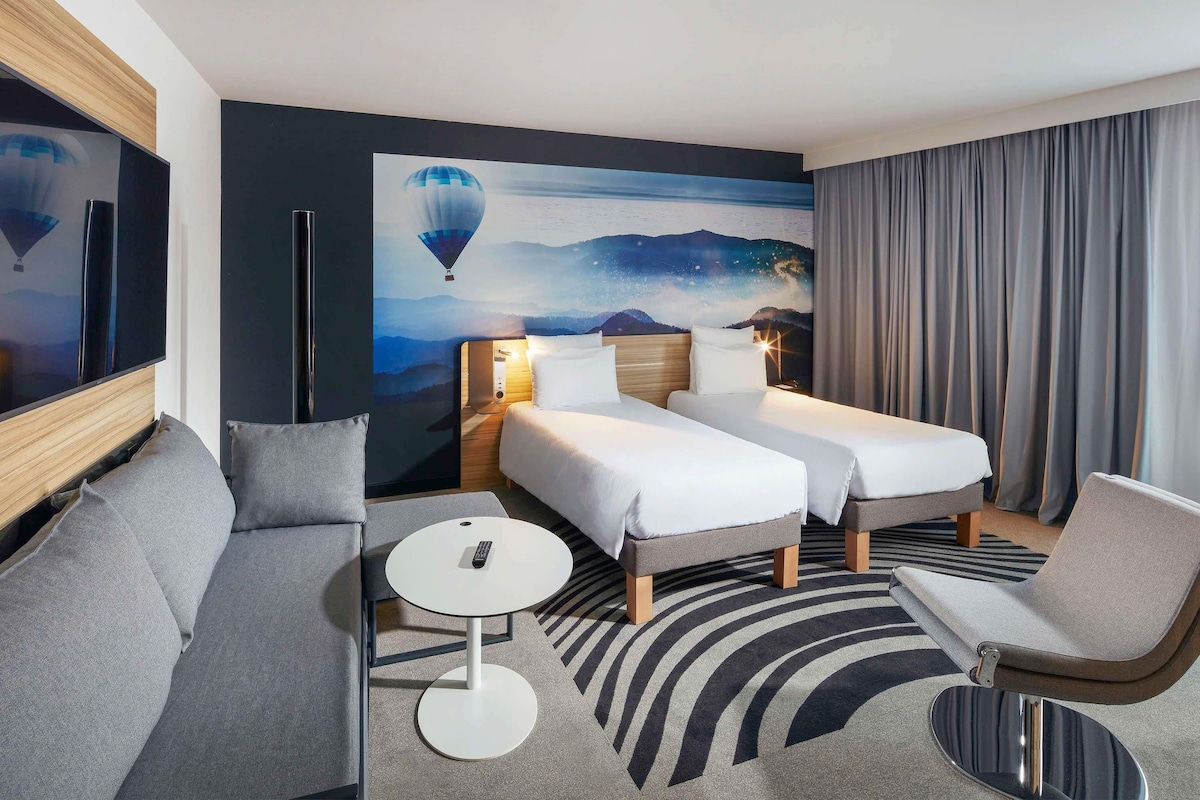 A hotel room with two beds, a sofa, a small round table, and a large TV.