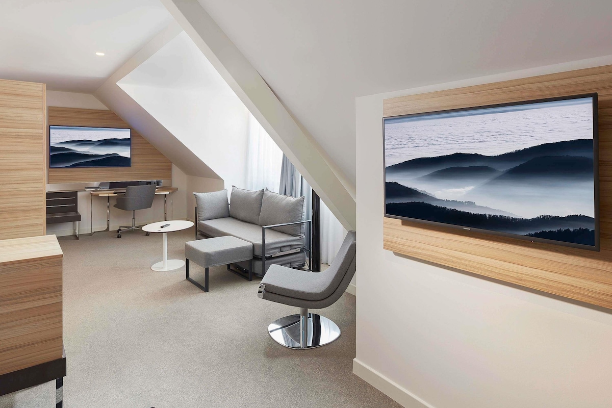A modern interior with a sofa, a chair, a desk, and a television mounted on the wall.