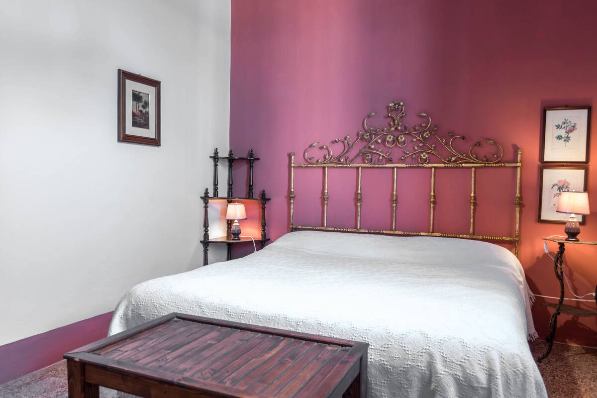 A bedroom with a bed, a bedside table, a lamp, and a picture frame on the wall.