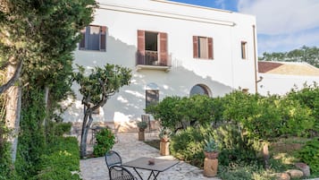 Un edificio blanco con balcón, sendero de piedra y zona de estar al aire libre con sillas y una mesa.