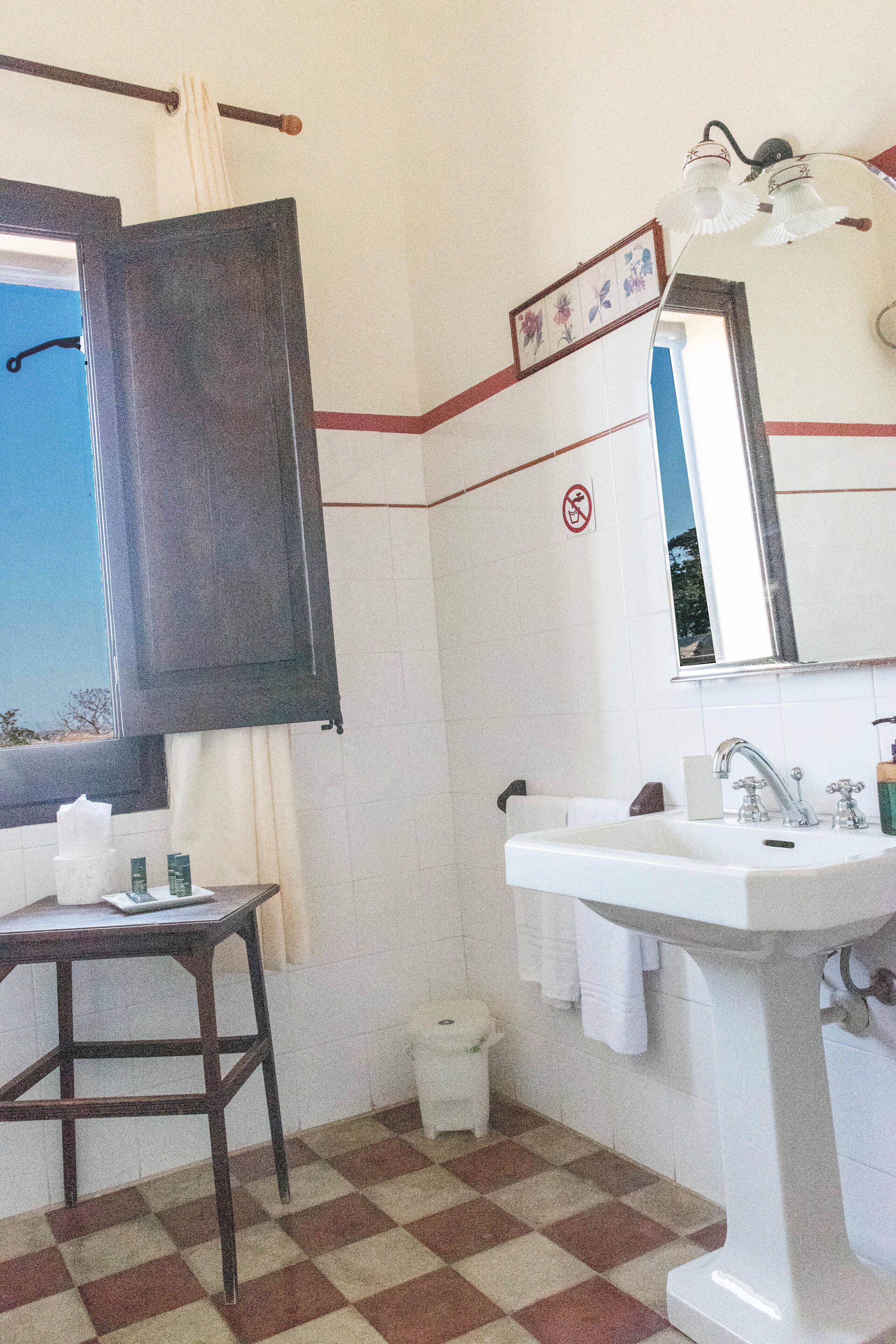 Une salle de bain avec un carrelage à motifs géométriques, un lavabo avec un miroir, un porte-serviettes et une fenêtre donnant sur un paysage agréable.
