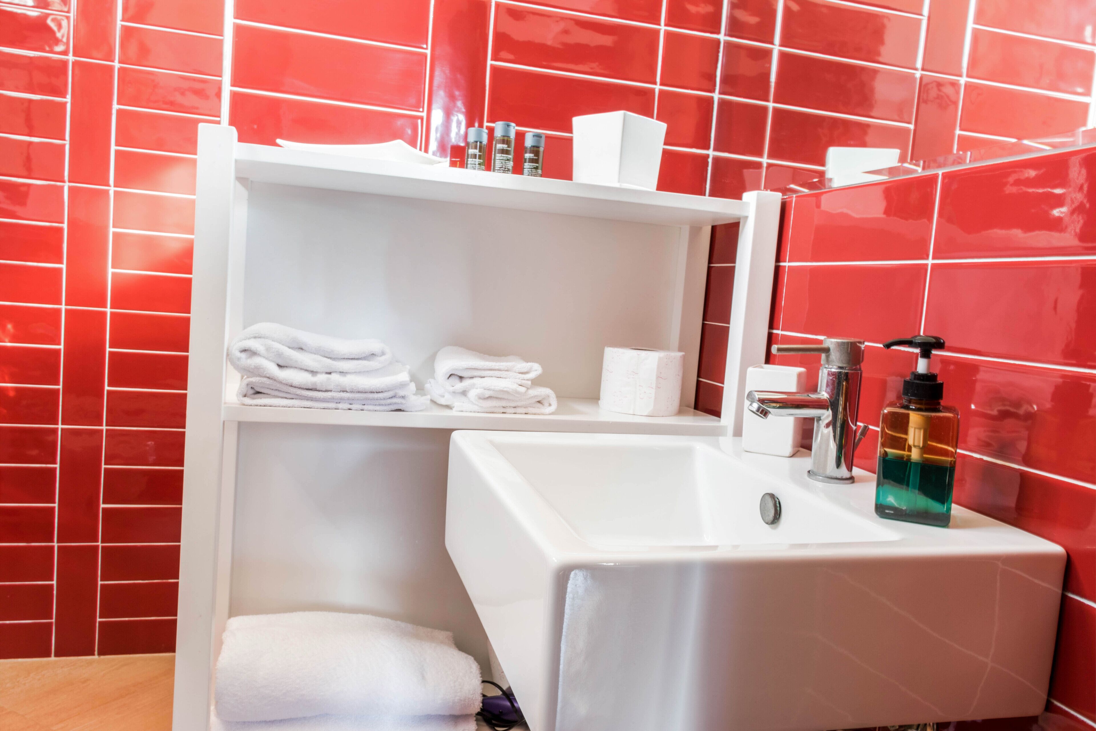 Un baño con lavamanos blanco, un espejo y una repisa con toallas dobladas y artículos de aseo.