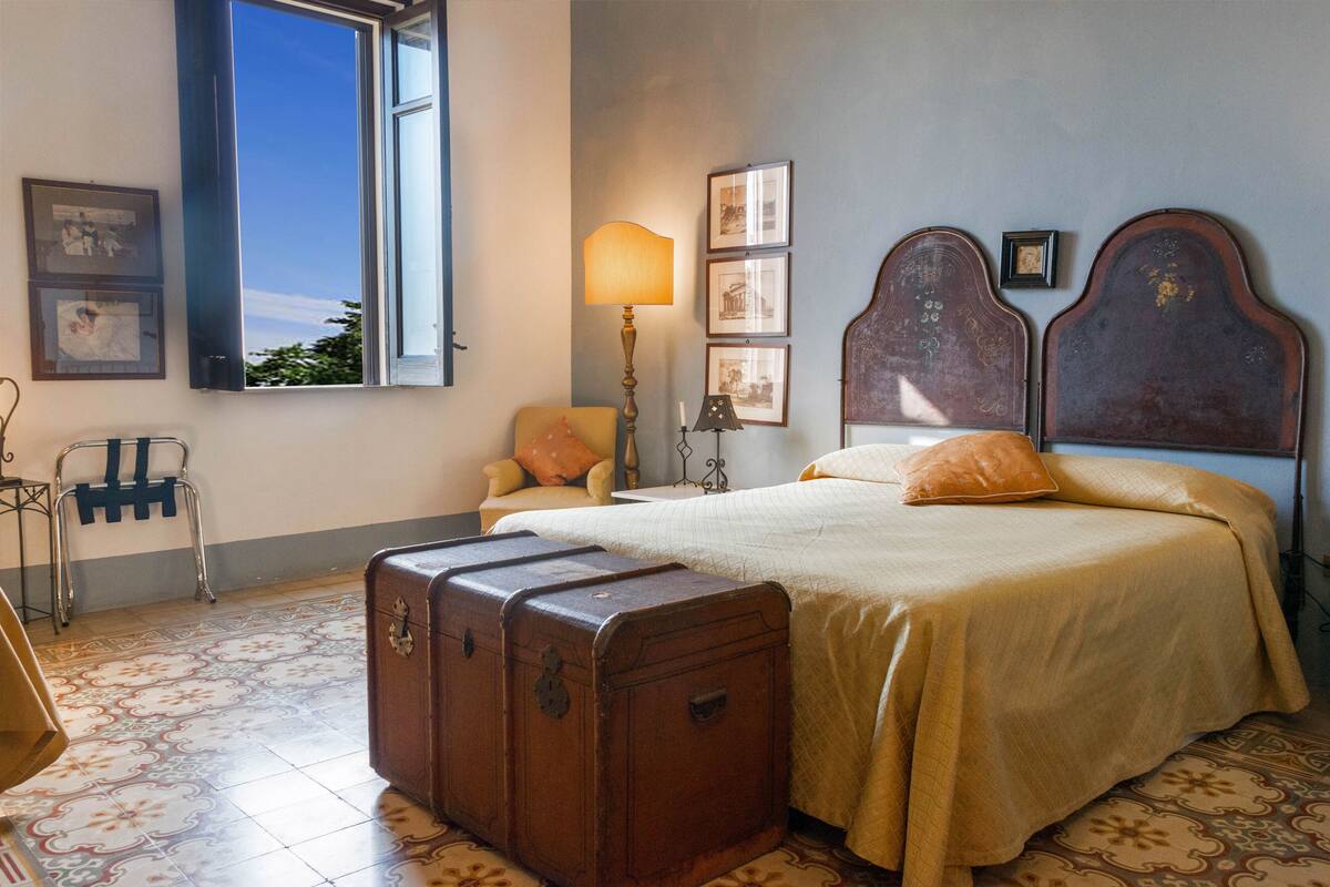 A bedroom with a bed, a suitcase, a chair, and a window with a view.