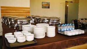 A buffet setup with stacked plates, bowls, and covered food containers. - The Prime Hotel Jaipur (Jaipur)