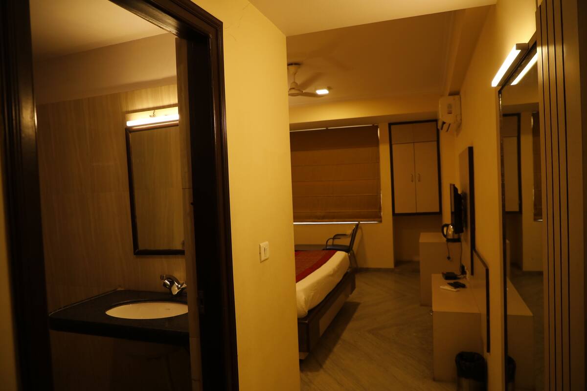 Une chambre d’hôtel de taille réduite, comprenant un lit simple, une table de chevet, un petit bureau, un miroir et une salle de bain avec un lavabo et des toilettes.