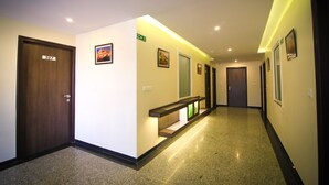 A hotel hallway with a wooden door labeled 307, a bench with a green sign, and framed pictures on the walls. - The Prime Hotel Jaipur (Jaipur)