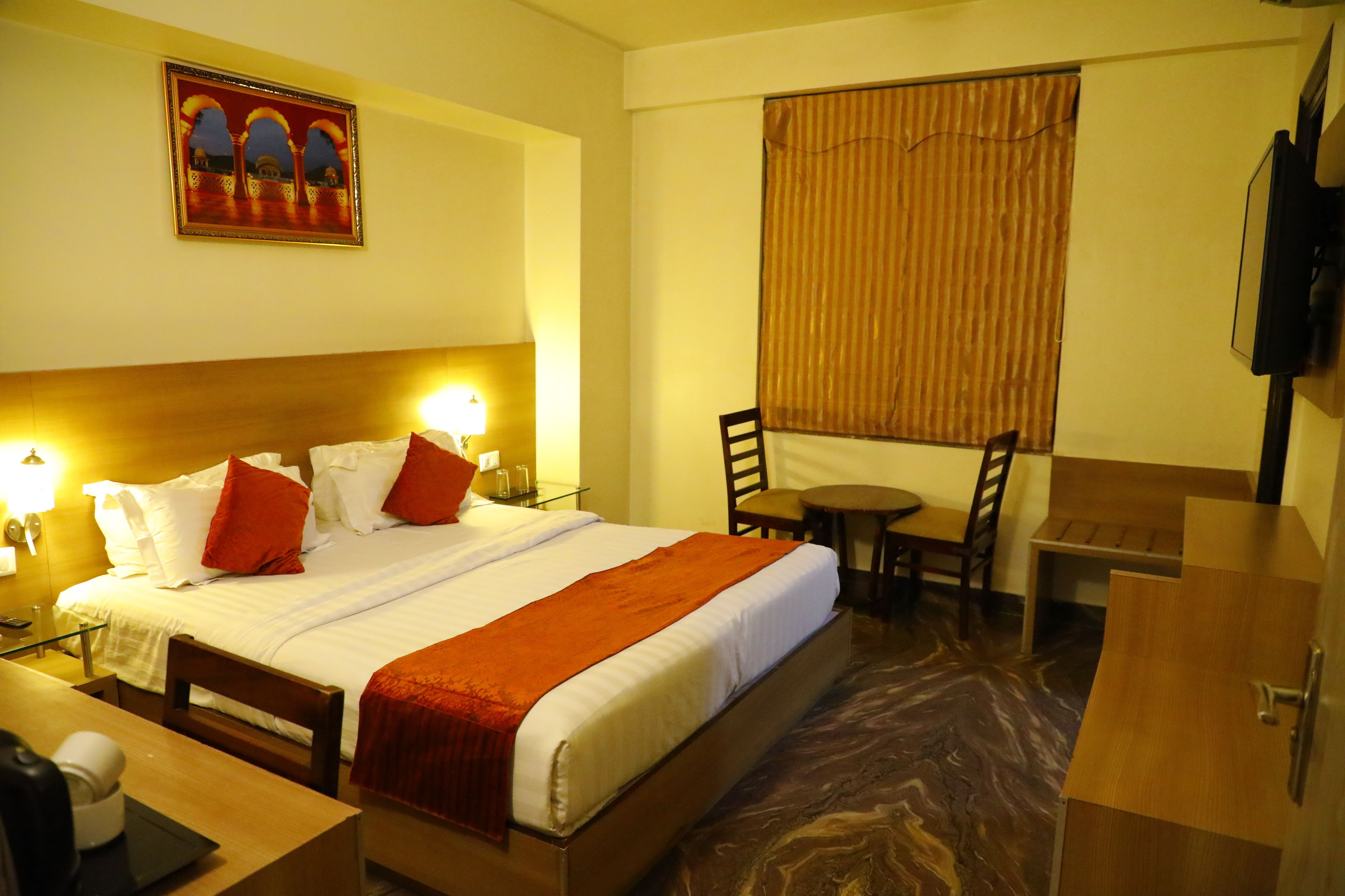 Een hotelkamer met een bed, nachtlampen, een bureau met stoel, een kleine tafel en een televisie aan de muur.