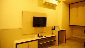 A hotel room with a flat-screen TV mounted on the wall, a small table with a kettle and a cup, and a wardrobe. - The Prime Hotel Jaipur (Jaipur)