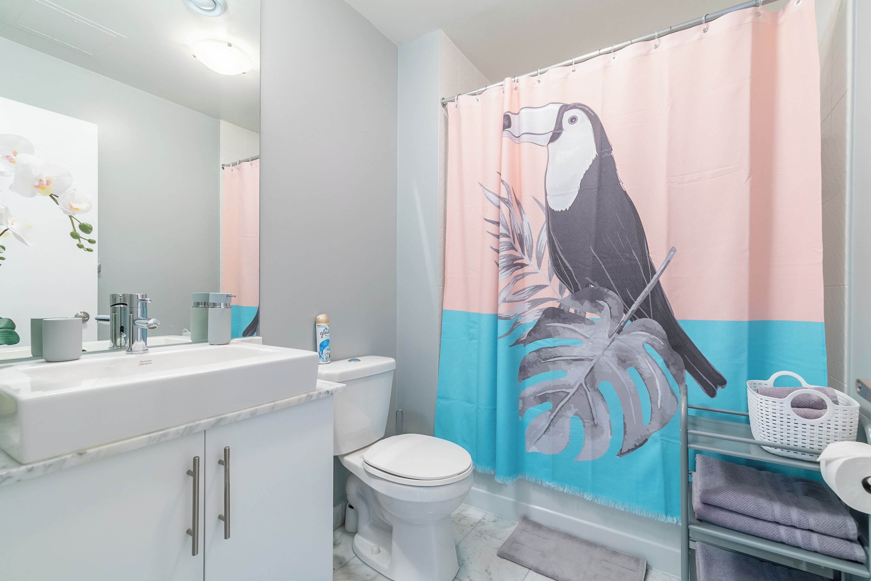 A bathroom with a white sink, toilet, and shower curtain featuring a toucan and leaf design.