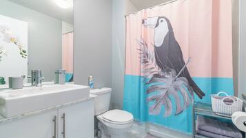 A bathroom with a white sink, toilet, and shower curtain featuring a toucan and leaf design.