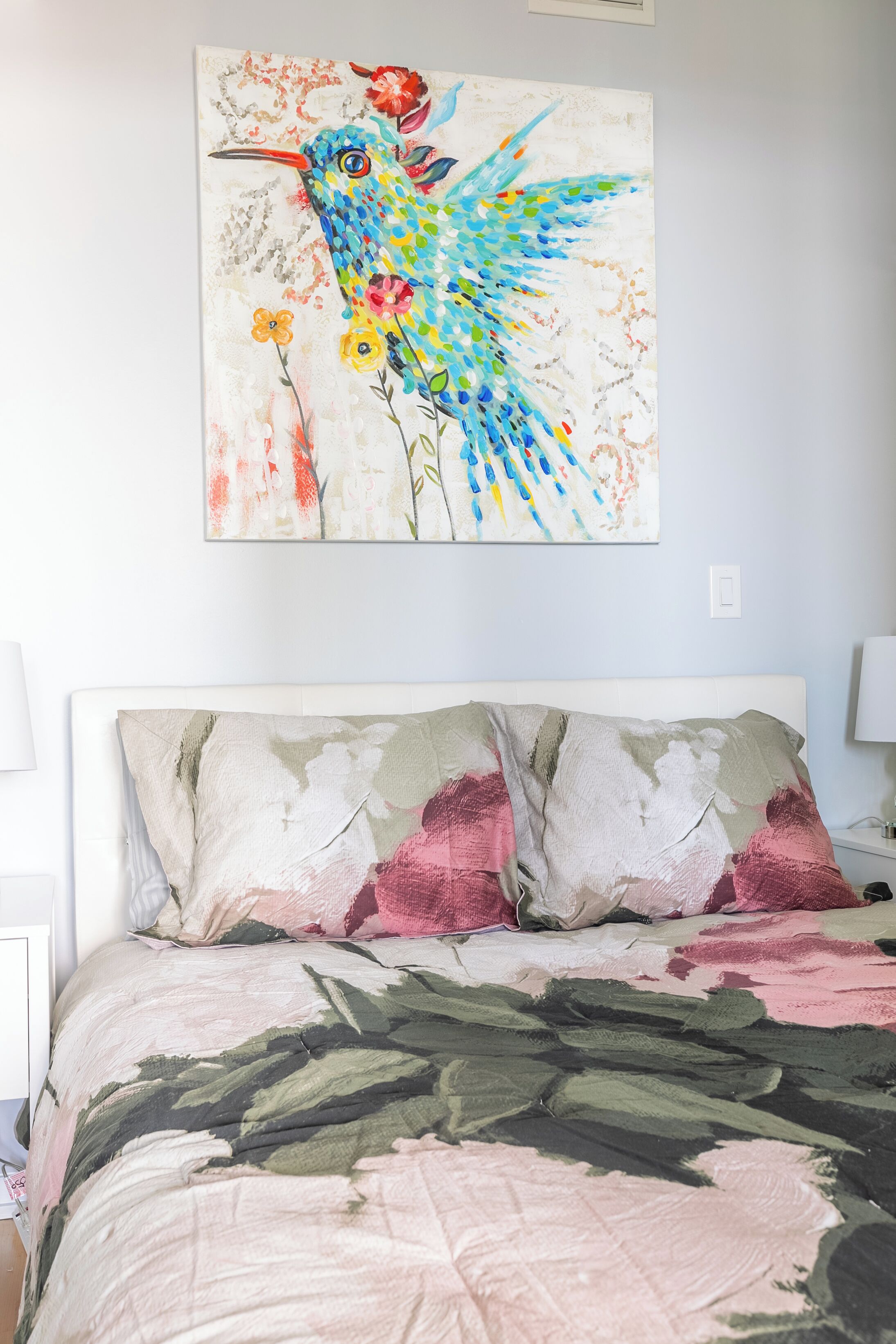 Une chambre à coucher avec un lit, des oreillers et un tableau représentant un oiseau, accroché au mur.