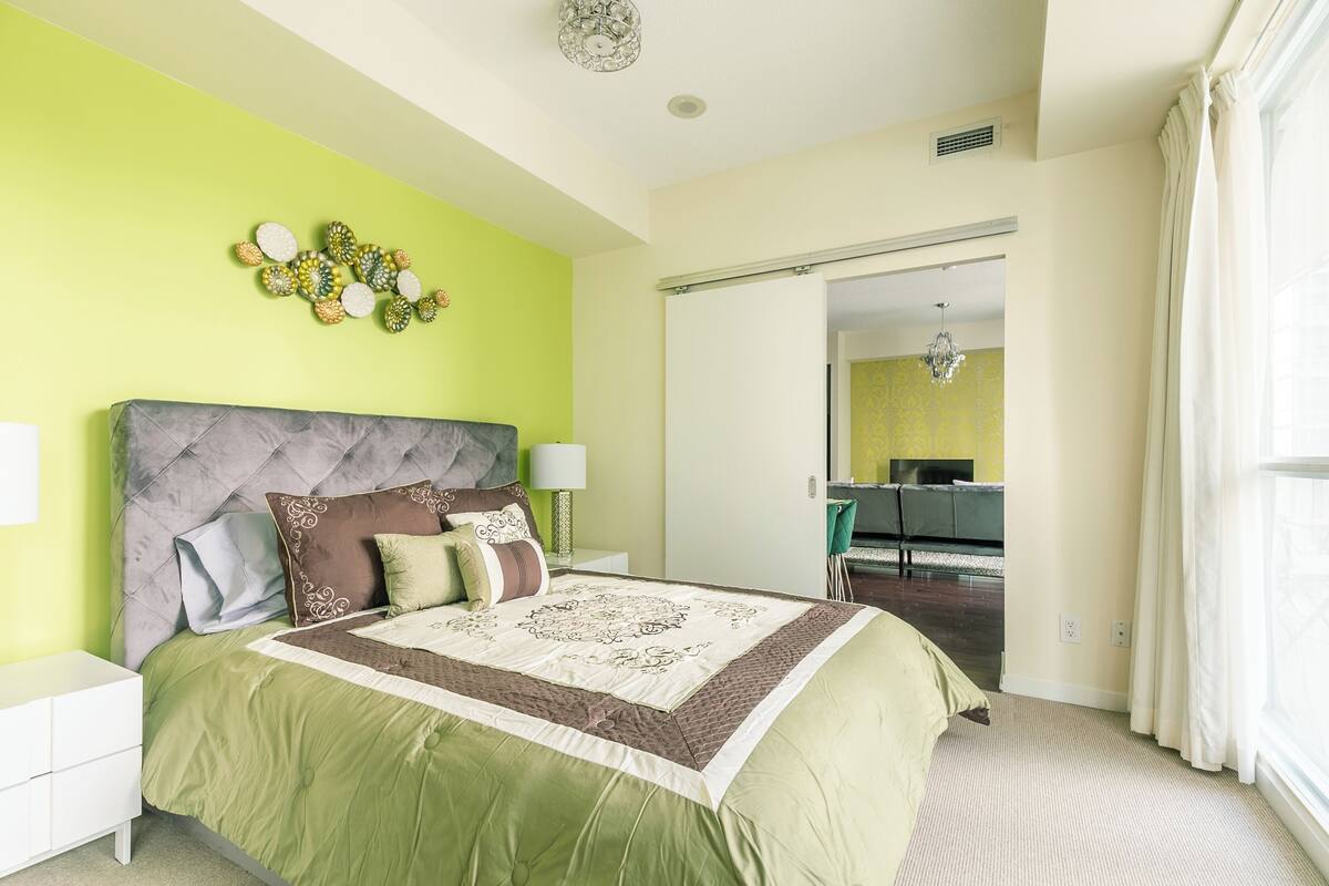Un dormitorio con una paleta de colores verde y blanco, un cabecero capitonado, un adorno en la pared y vistas al área de estar.