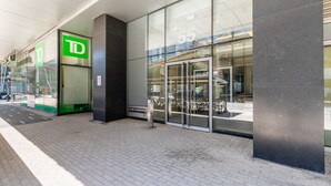 Ein modernes Gebäude mit Glasfassade, einem grünen 'TD'-Schild und einer Metallhaustür.