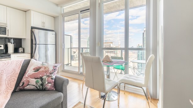 Eine moderne Küche mit weißen Schränken und Edelstahlgeräten, ein Essbereich mit einem Glastisch und Stühlen sowie große Fenster mit Blick auf die Stadt.