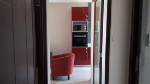 Corredor que dá para uma cozinha com armários vermelhos, micro-ondas e forno.