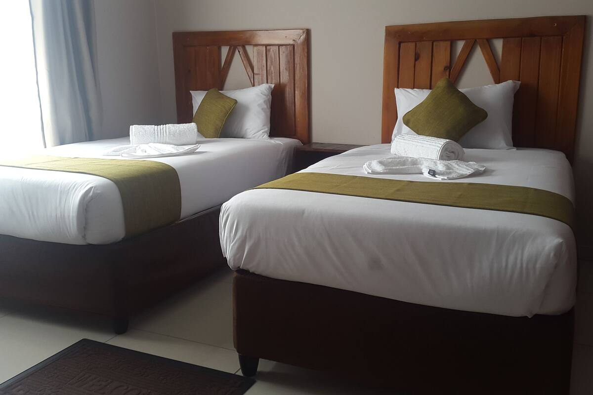 Two neatly made beds with white linens, green throw pillows, and a brown headboard.