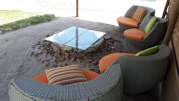 Uma área de pátio com móveis de vime, uma mesa de vidro e uma lareira de pedra.