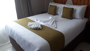 Cama bem arrumada com lençóis brancos, duas almofadas marrons e um cobertor dourado.