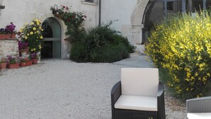 Une cour avec des espaces de repos en plein air, des plantes en pot et un bâtiment doté d’une façade en pierre.
