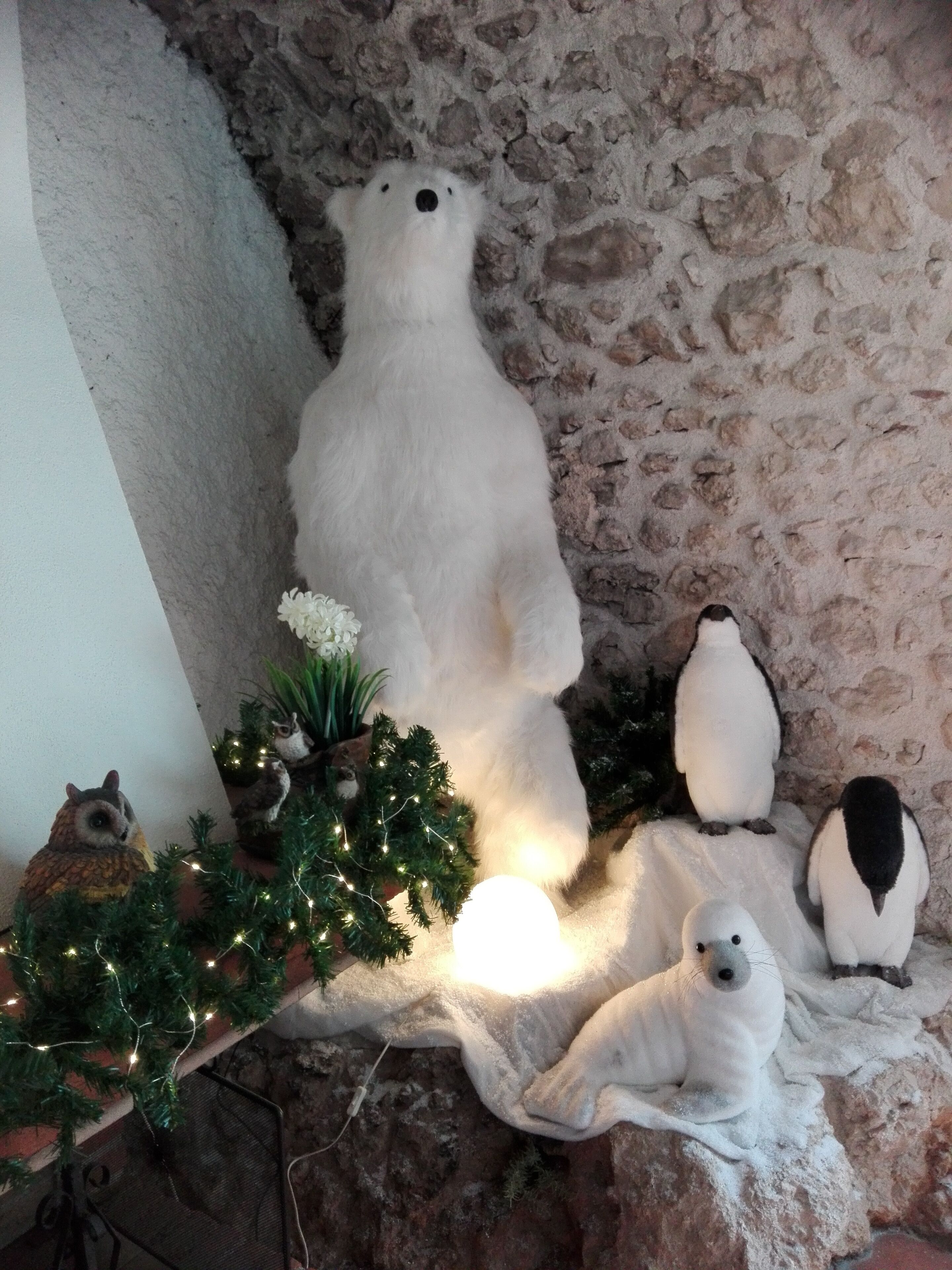 Eine Eisbärenstatue, ein Weihnachtsbaum und Pinguinfiguren in einem Raum mit einer Steinwand.