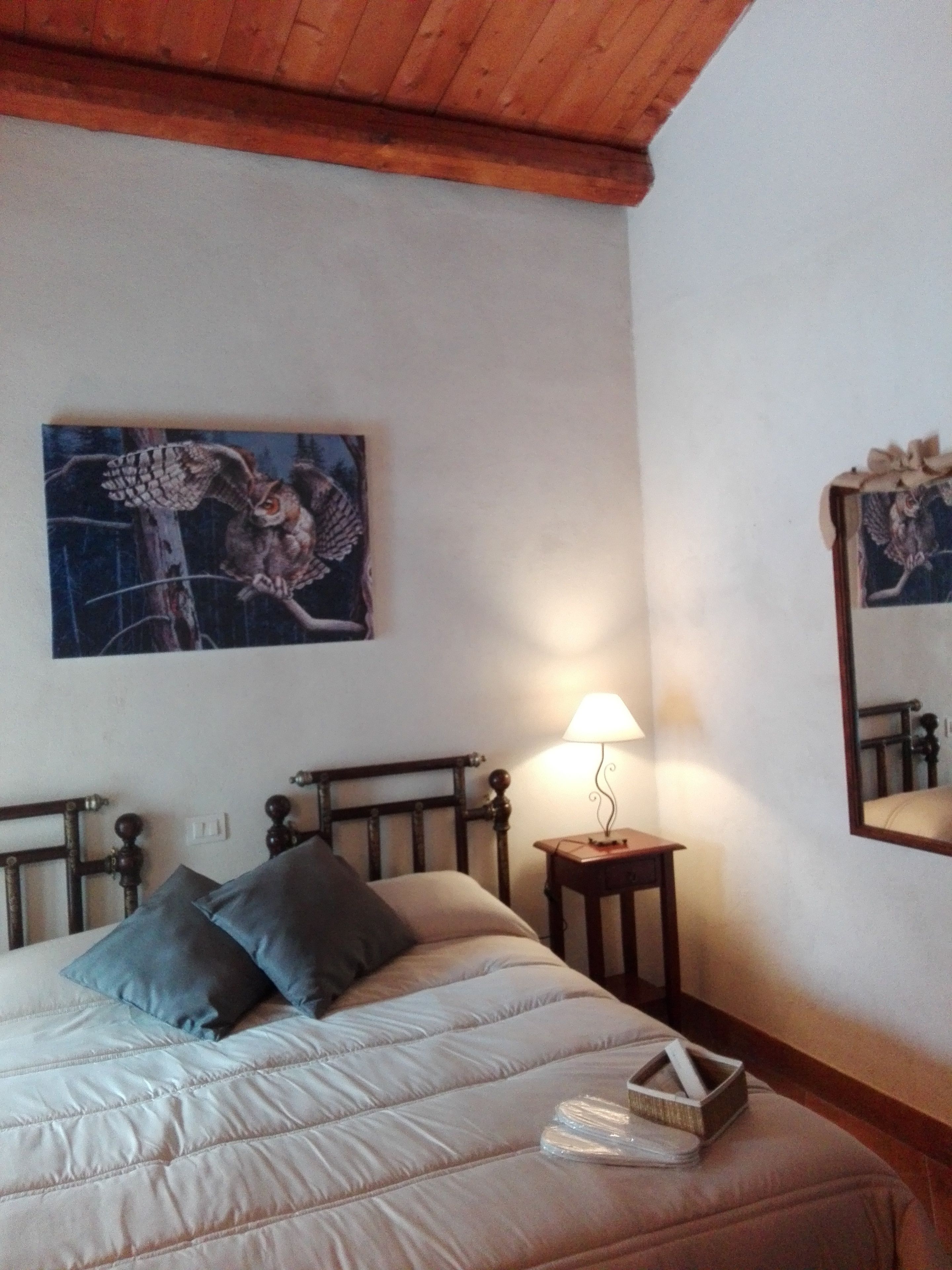 Ein Schlafzimmer mit Bett, Kissen, einer Nachttischlampe, einem Wandbild und einem Spiegel.
