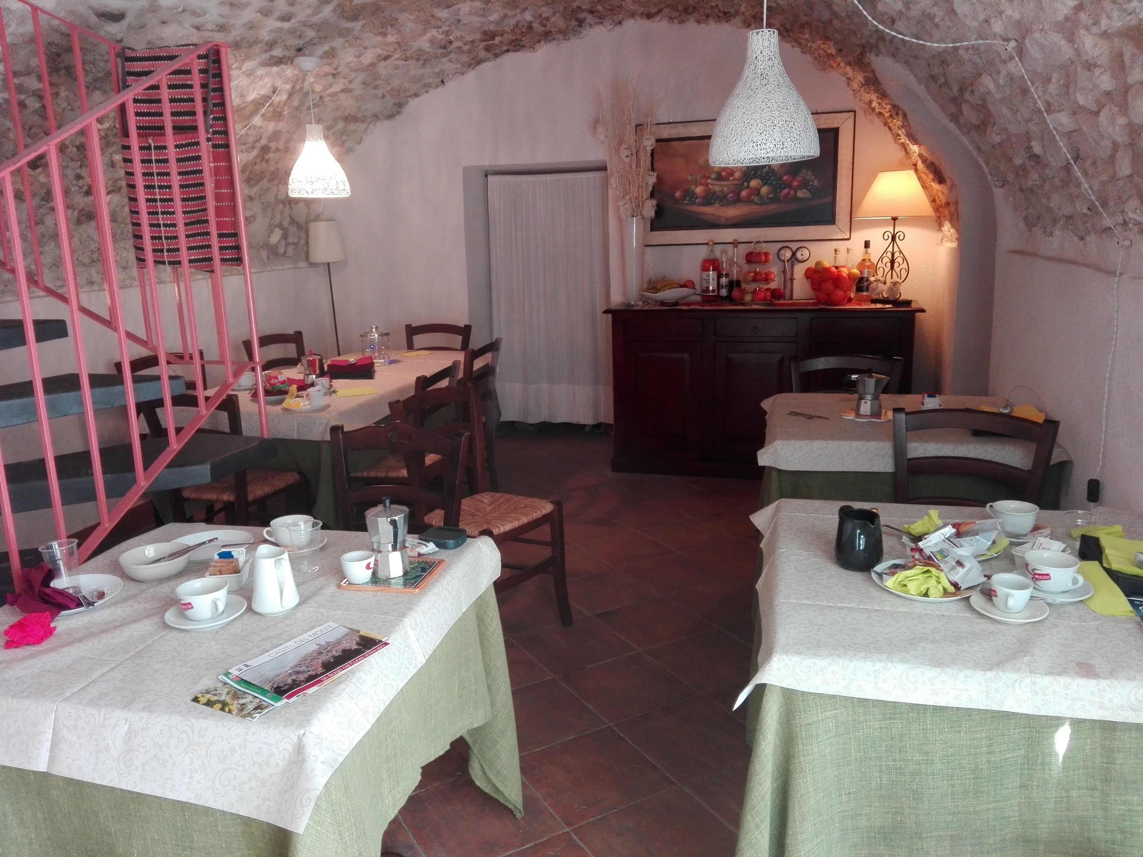 A dining area with two tables set for meals, a staircase, and a kitchen in the background.