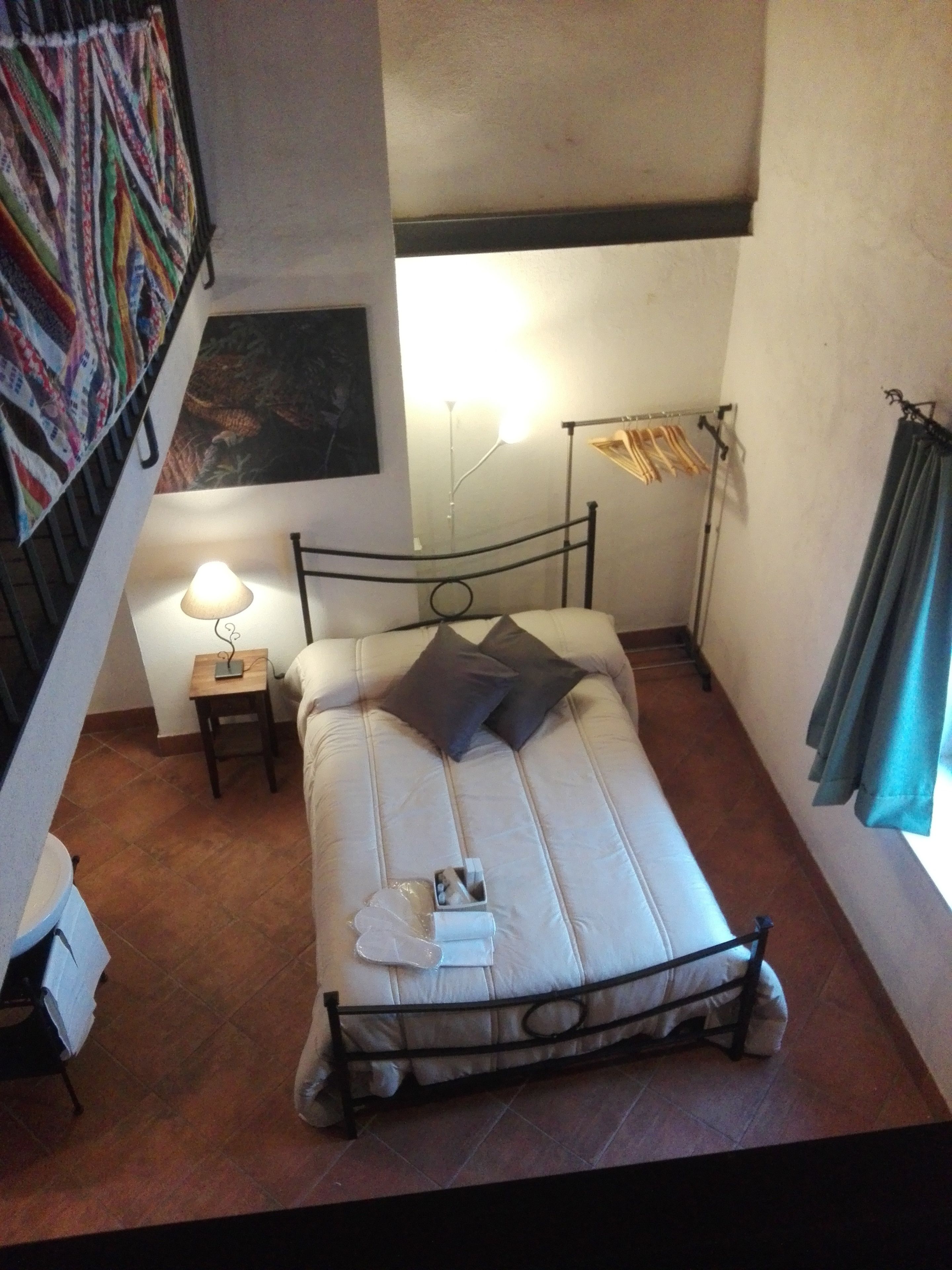 A small, cozy bedroom with a single bed, a bedside table with a lamp, and a wall-mounted shelf.