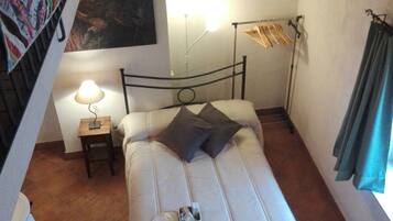 A small, cozy bedroom with a single bed, a bedside table with a lamp, and a wall-mounted shelf.
