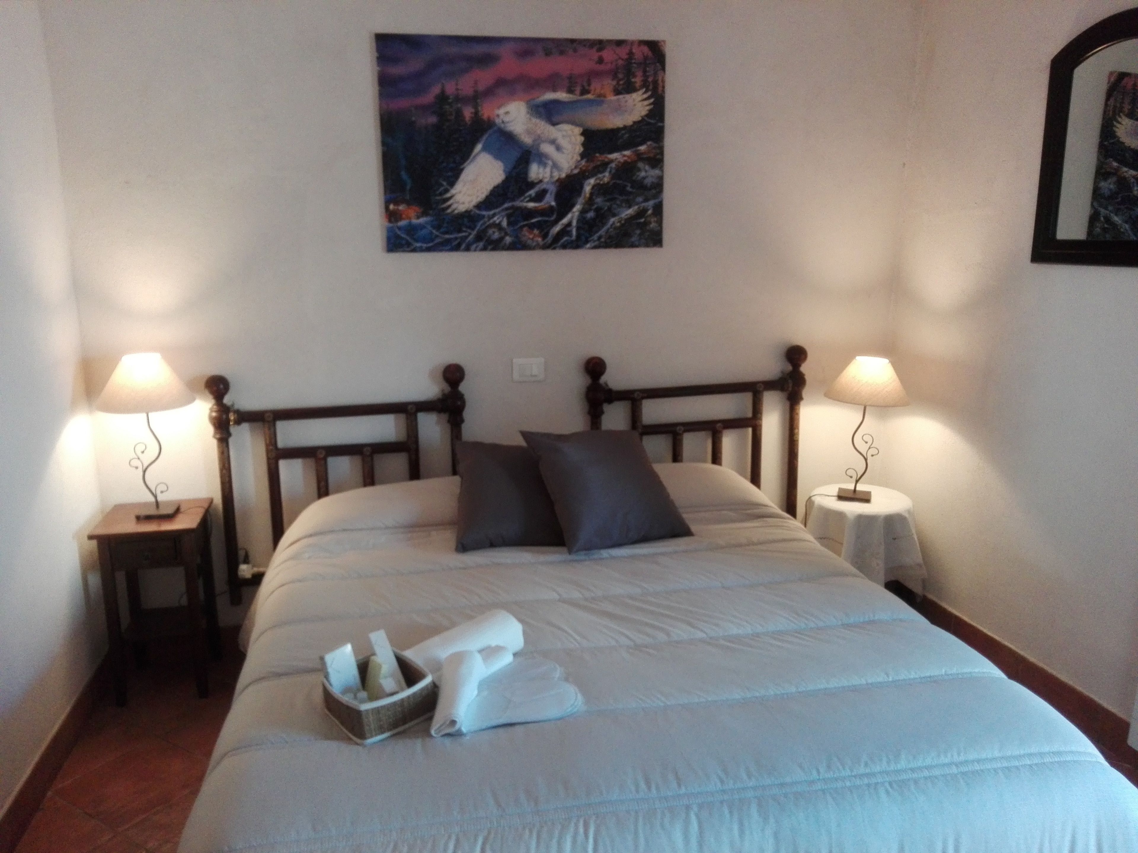 Una cama bien hecha con almohadas, una mesita de noche con lámpara y un cuadro en la pared.