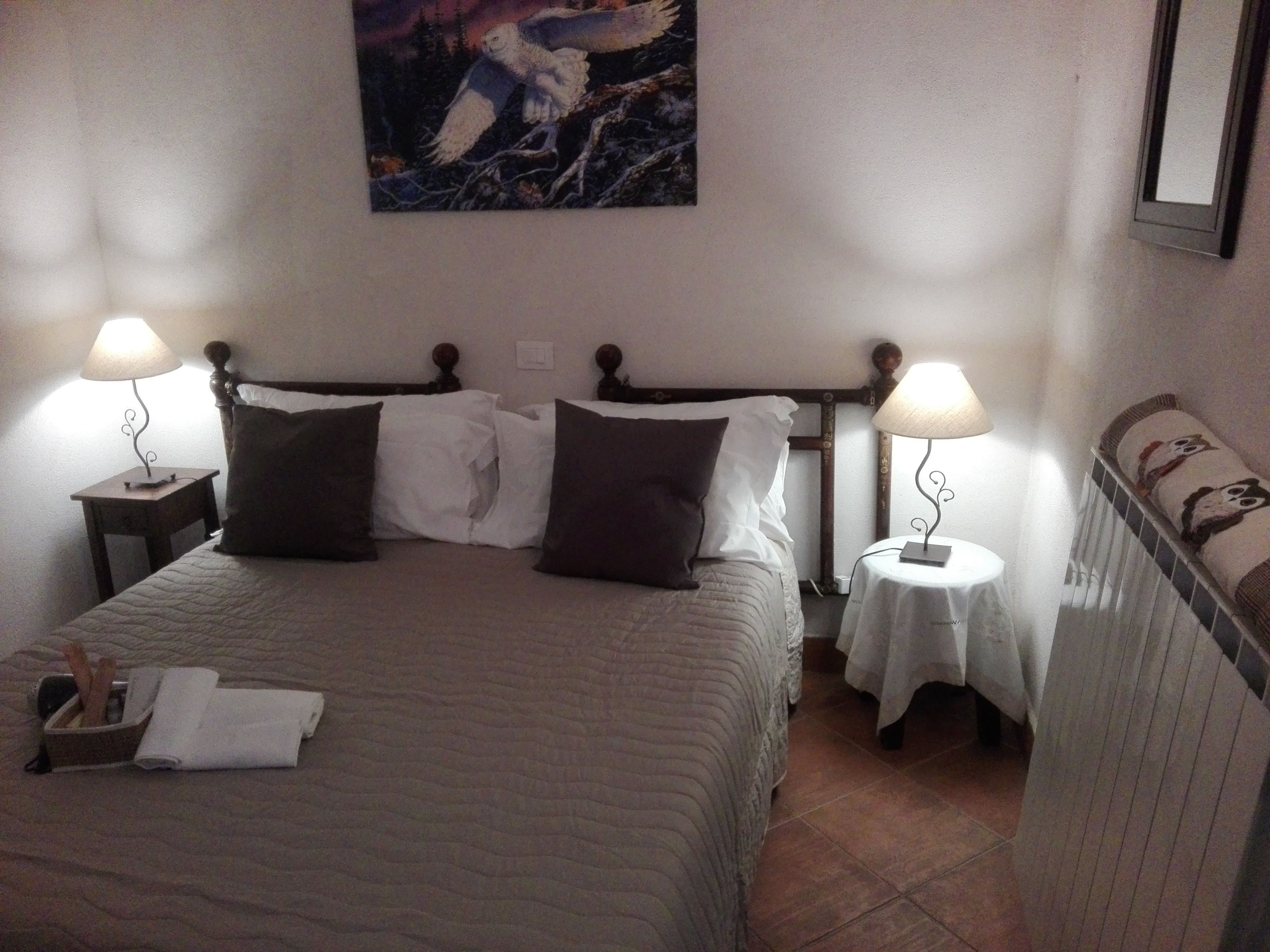 A hotel room with a bed, two bedside tables with lamps, a painting on the wall, and a chair with a cushion.